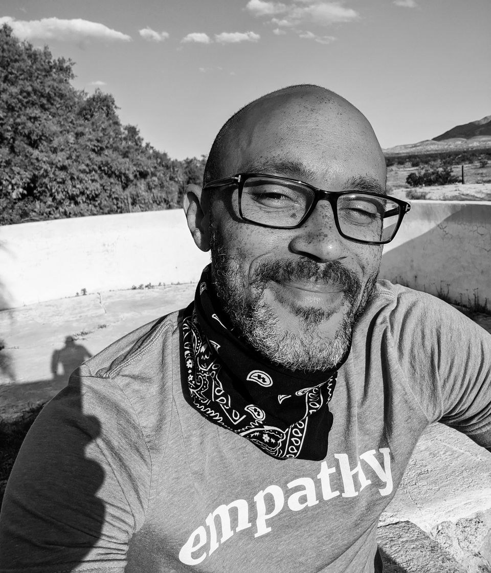 Shelton Davis smiling outdoors in glasses, a bandana and an "empathy" T-shirt